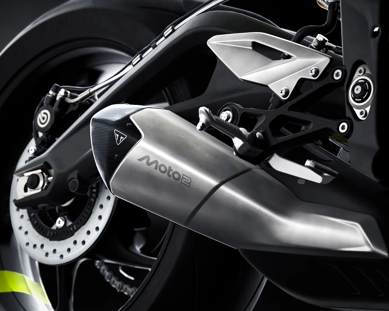 Close-up of a silver Moto2 motorcycle exhaust pipe with carbon fiber tip and rear brake disc.