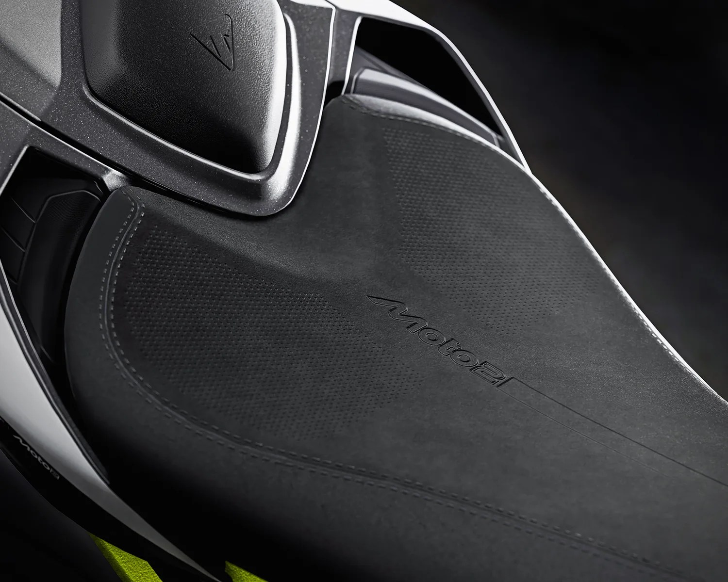 Close-up of a black textured motorcycle seat with "moto2" embossed on it and a black handlebar grip nearby.