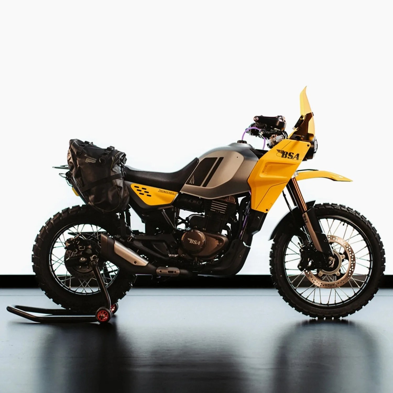Yellow and gray BSA adventure motorcycle with knobby tires and black saddlebag on rear wheel stand.