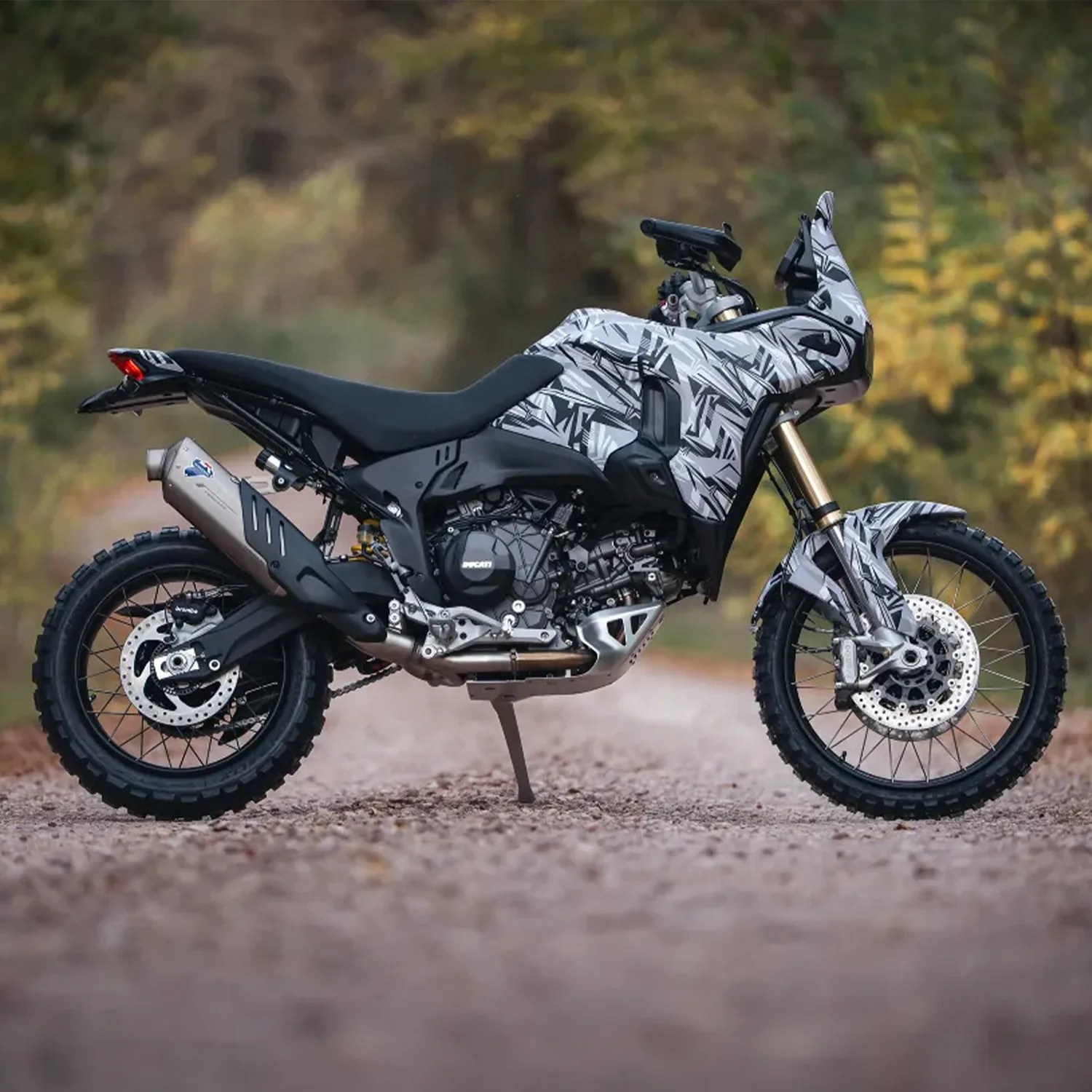Adventure motorcycle with black and white geometric camouflage pattern parked on a gravel road.