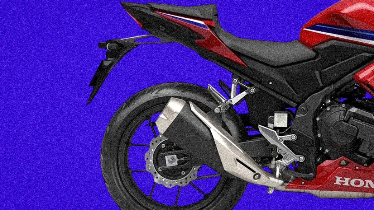 Rear side view of a red Honda motorcycle showing the rear wheel, exhaust, and part of the seat against a blue background.