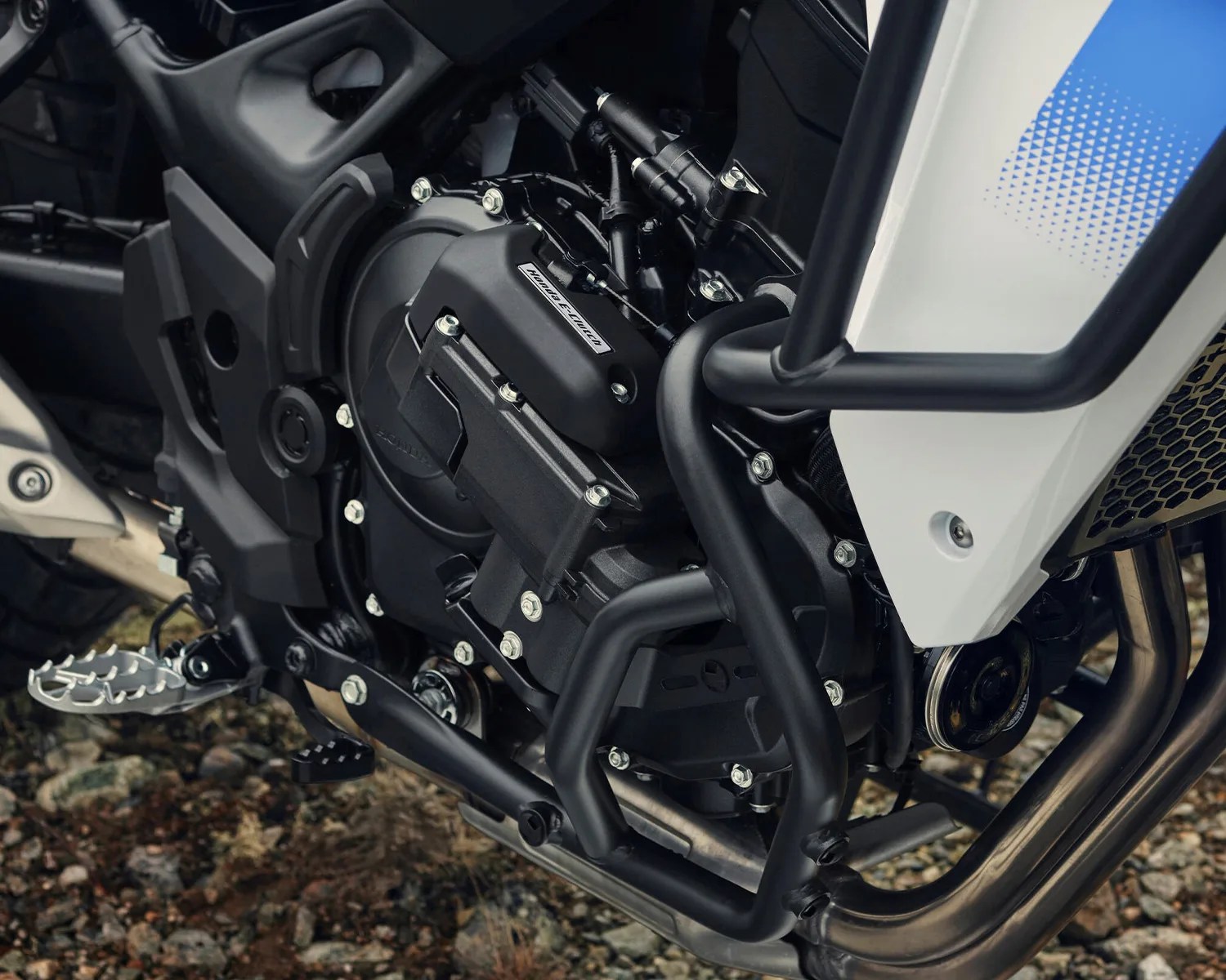 Close-up of a black motorcycle engine with protective crash bars and a white and blue fairing panel.
