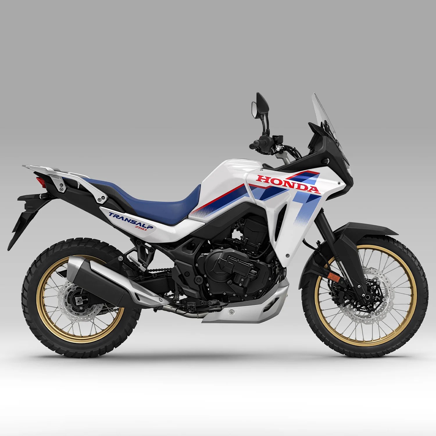White Honda Transalp 750 adventure motorcycle with blue seat and gold rims on gray background.