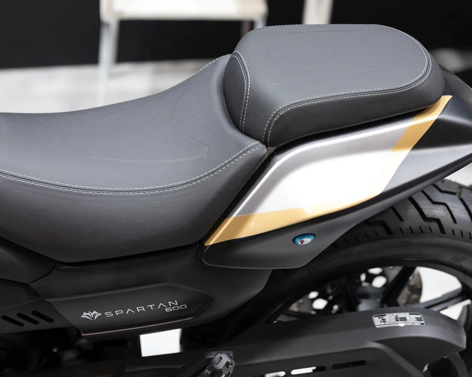 Close-up of a black and gray motorcycle seat with white stitching and "SPARTAN 600" branding on the side panel.