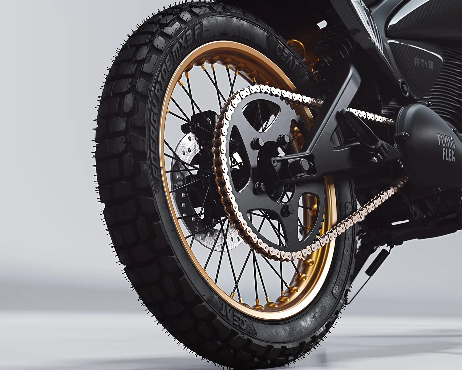 Rear wheel of a motorcycle with knobby tire, gold rim, black spokes, and a silver chain on a black sprocket.