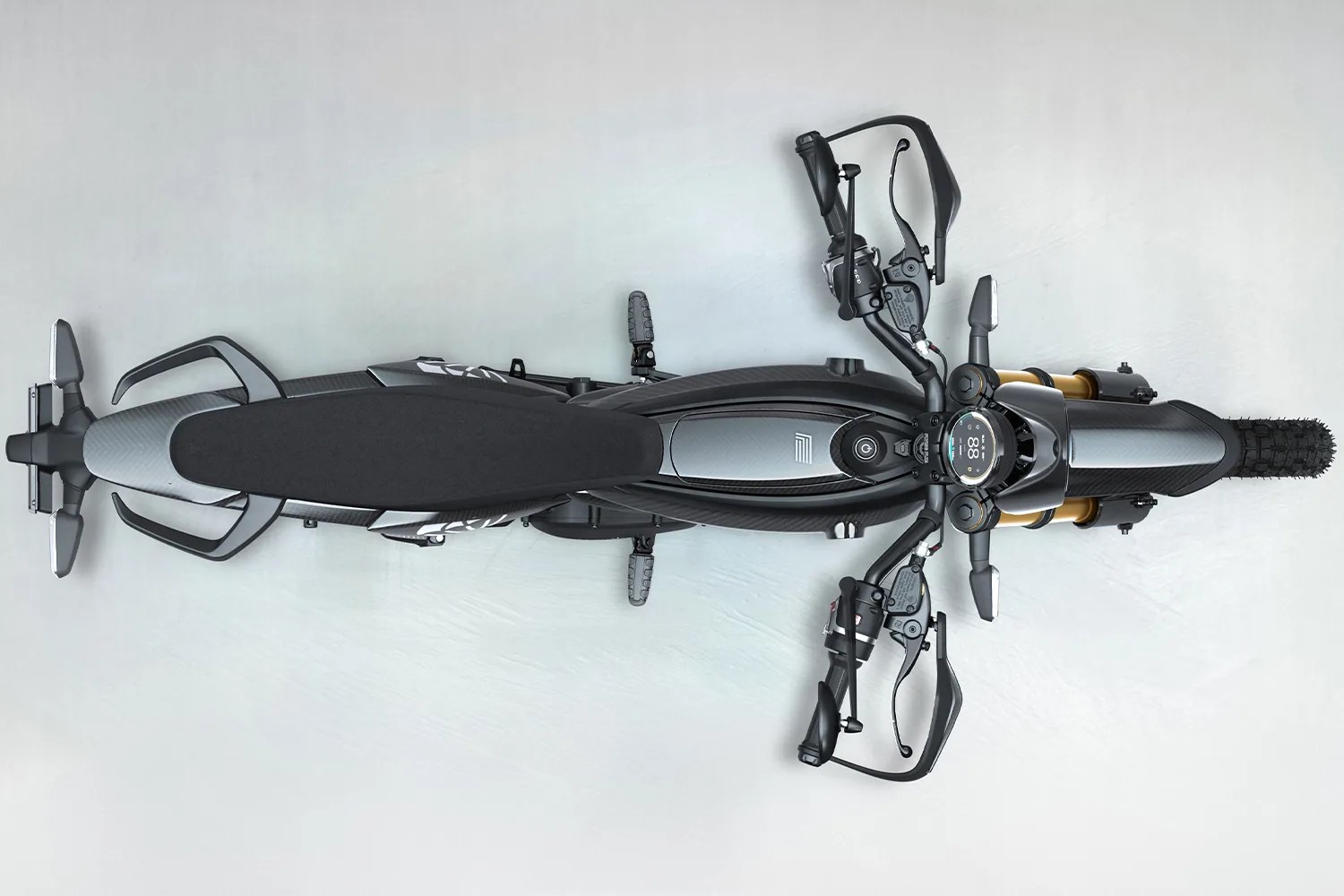 Top-down view of a black and gray electric motorcycle with digital display and knobby front tire on a light gray floor.