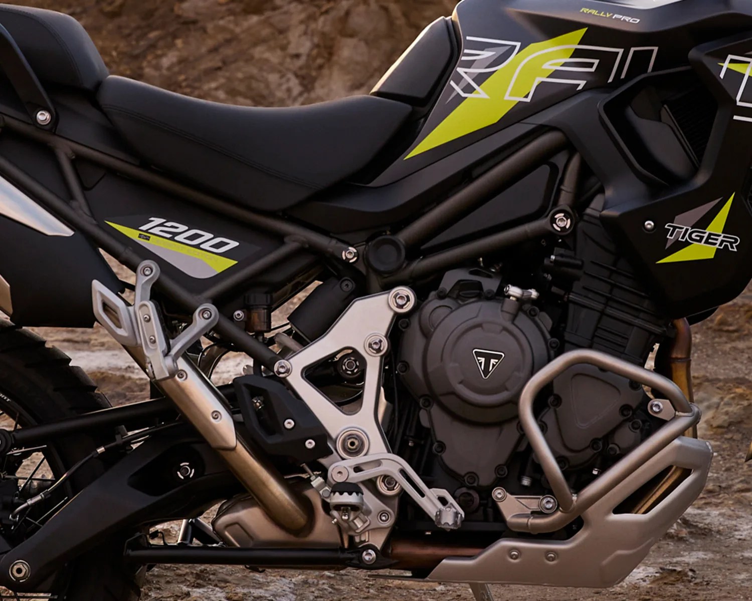 Close-up of a black and silver Triumph Tiger 1200 motorcycle engine and frame with yellow accents.
