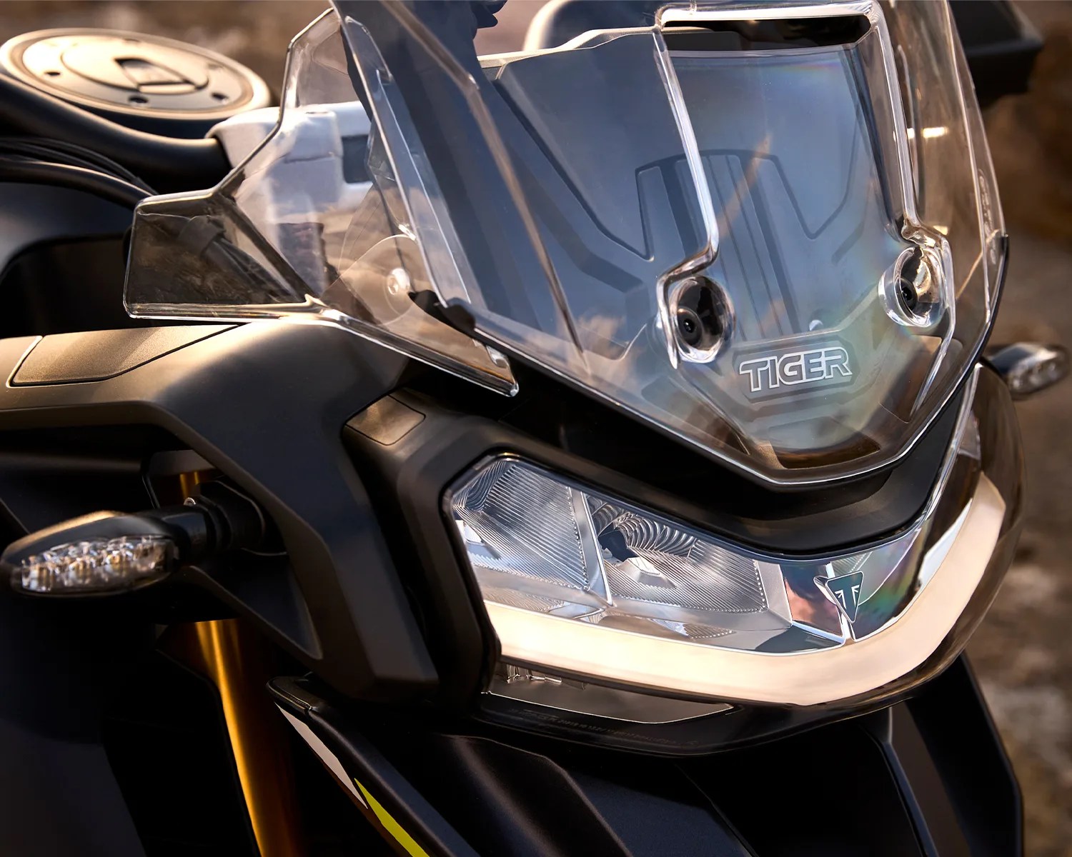 Close-up of a black motorcycle front with clear windshield labeled "TIGER" and angular headlight with Triumph logo.