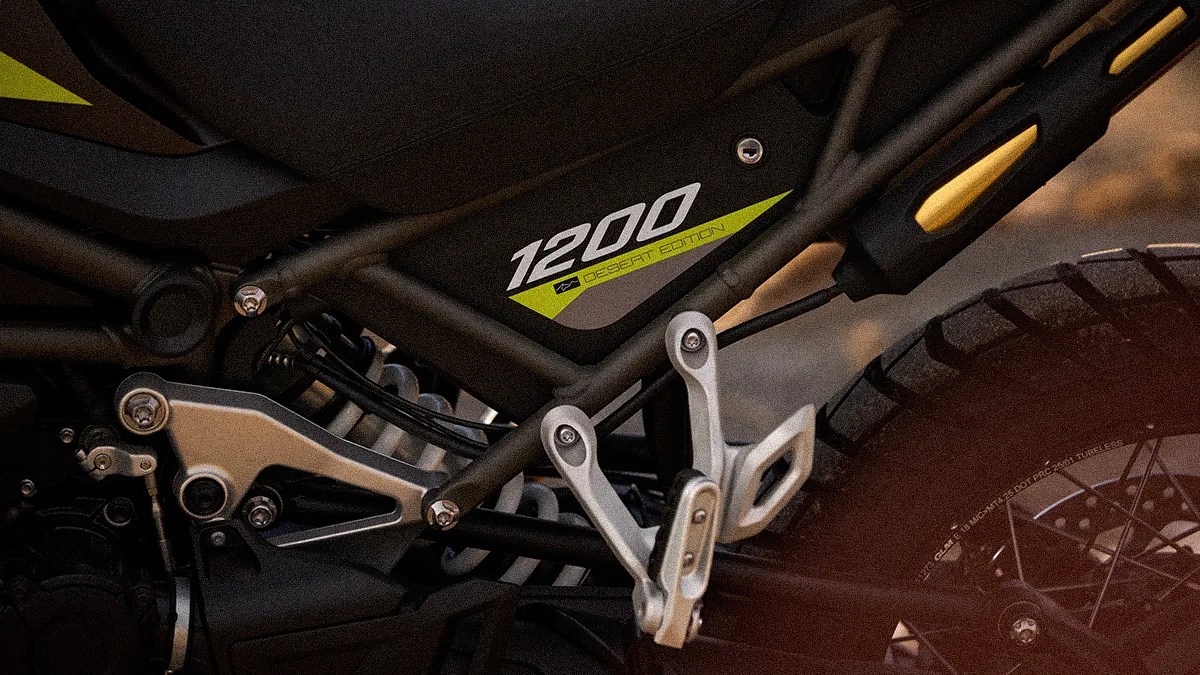 Close-up of a black motorcycle frame with "1200 Desert Edition" decal and rear tire with knobby tread.