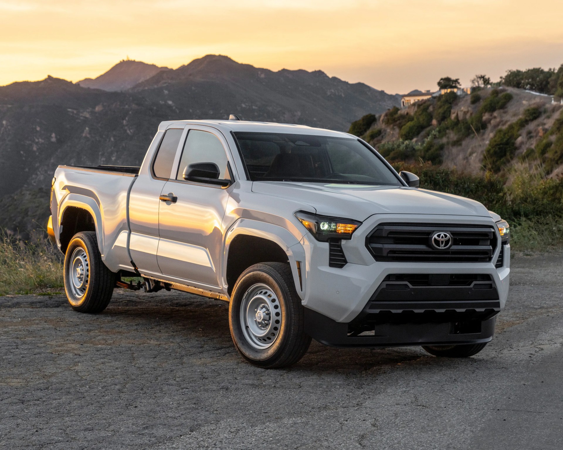 White Toyota pickup truck with black grille and steel wheels parked on a mountain road at sunset.