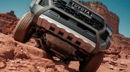 Front underside view of a gray Toyota truck navigating rocky red terrain with large tires and skid plates.