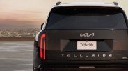 Rear view of a black Kia Telluride SUV with illuminated vertical taillights at sunset.