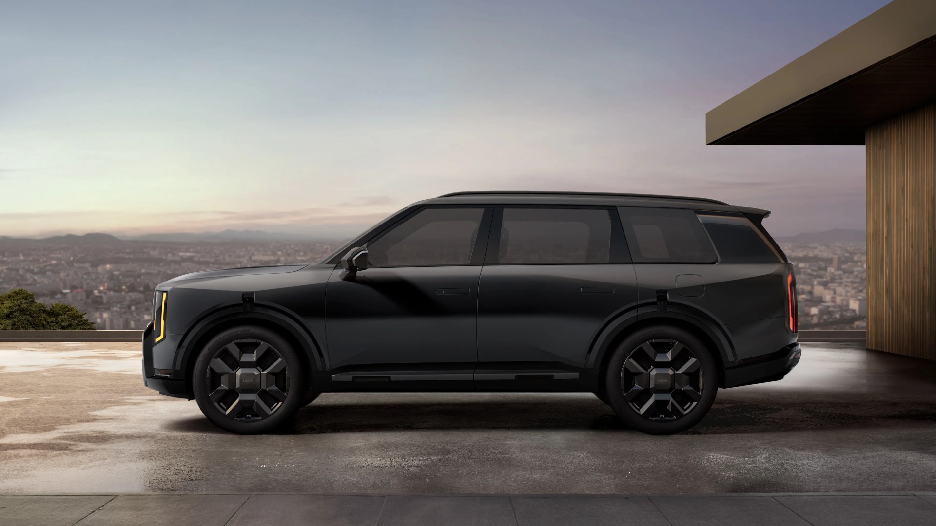 Black modern SUV with tinted windows parked on a rooftop with a cityscape background at dusk.
