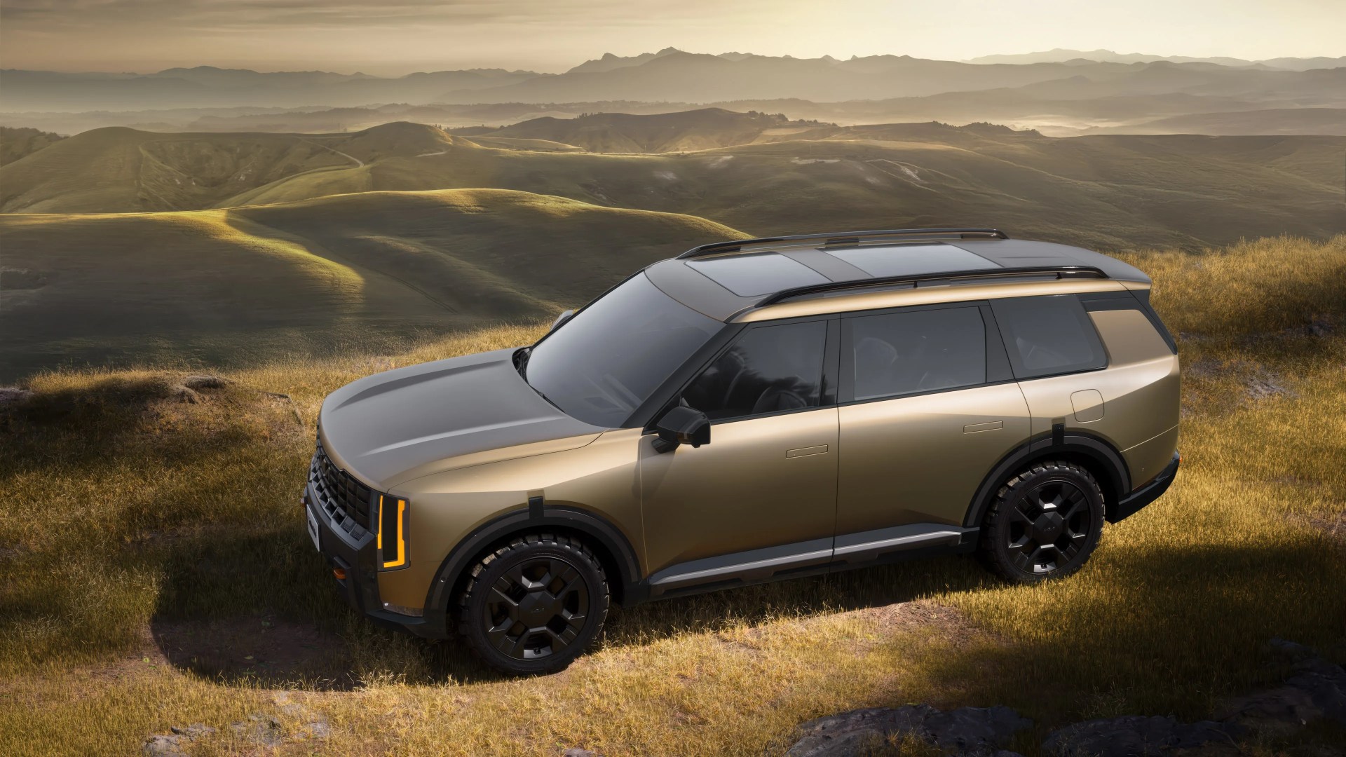Metallic bronze SUV with black roof and tinted windows parked on grassy terrain with hills in the background.