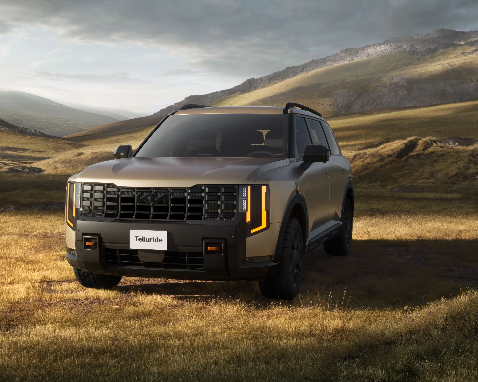 Matte gold Kia Telluride SUV with black grille and amber daytime running lights parked on grassy terrain with hills in the background.
