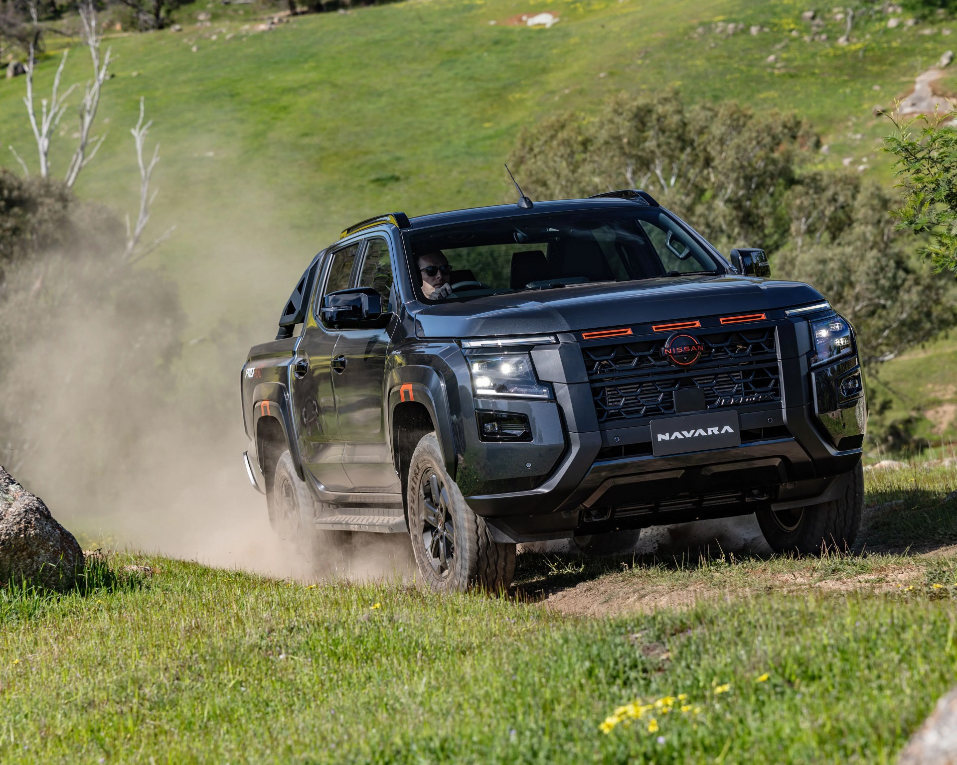 Black Nissan Navara pickup truck driving on a dusty grassy off-road trail.