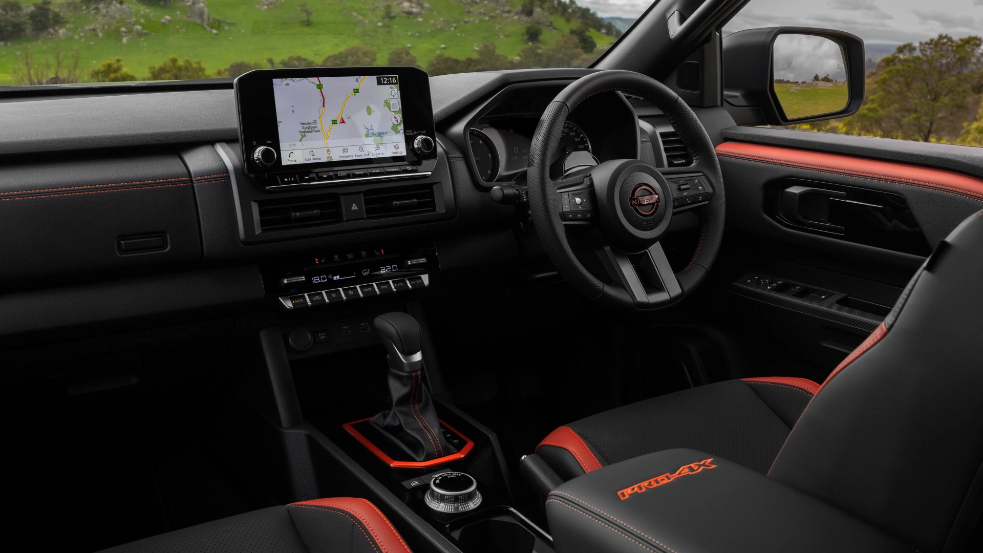 Black and red Nissan Pro-4X car interior with touchscreen navigation, leather-wrapped steering wheel, and gear shift.
