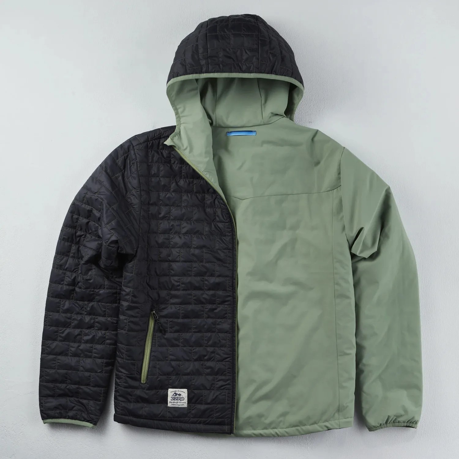 Two-tone jacket with black quilted left side and hood, and olive green smooth right side and sleeve, laid flat.