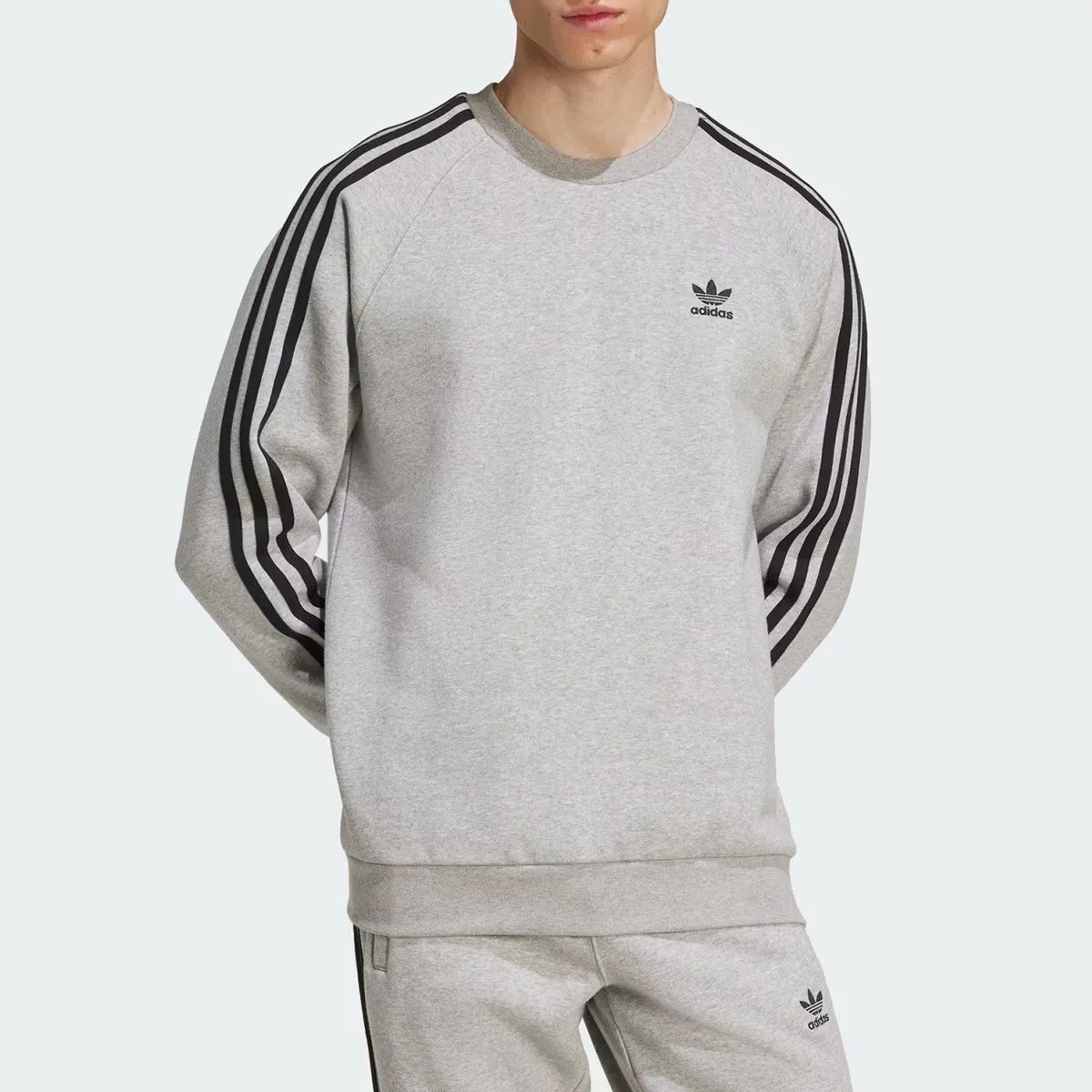 Light gray Adidas sweatshirt with black three stripes on sleeves and small black logo on chest.