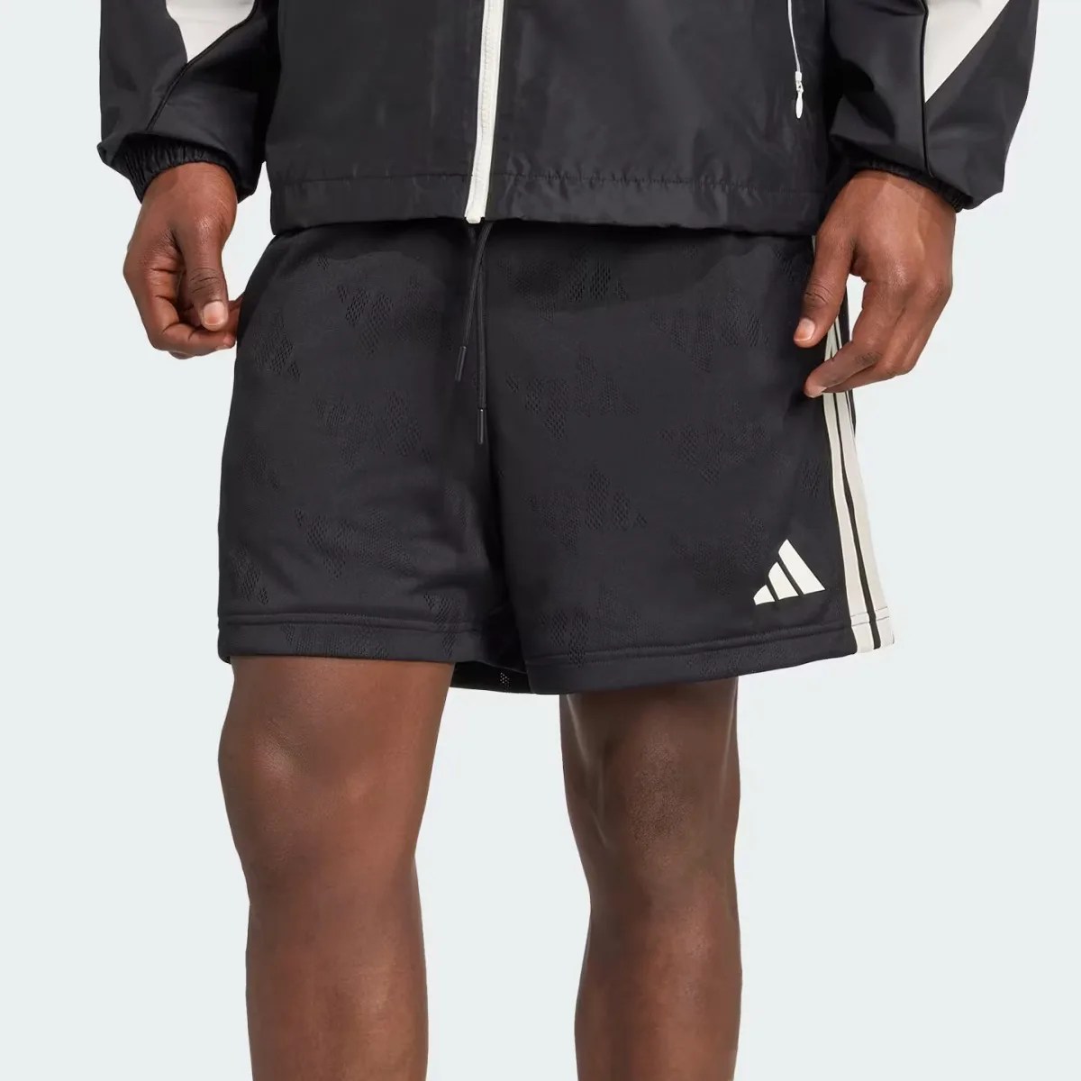Black athletic shorts with subtle pattern, white Adidas logo, and white side stripes worn by a person.
