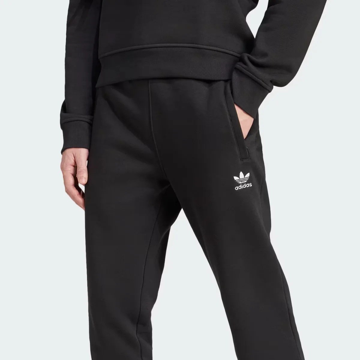 Black Adidas sweatpants with white trefoil logo on the left thigh, worn with a matching black sweatshirt.