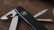 Black Swiss Army knife with multiple stainless steel tools extended on a wooden surface.