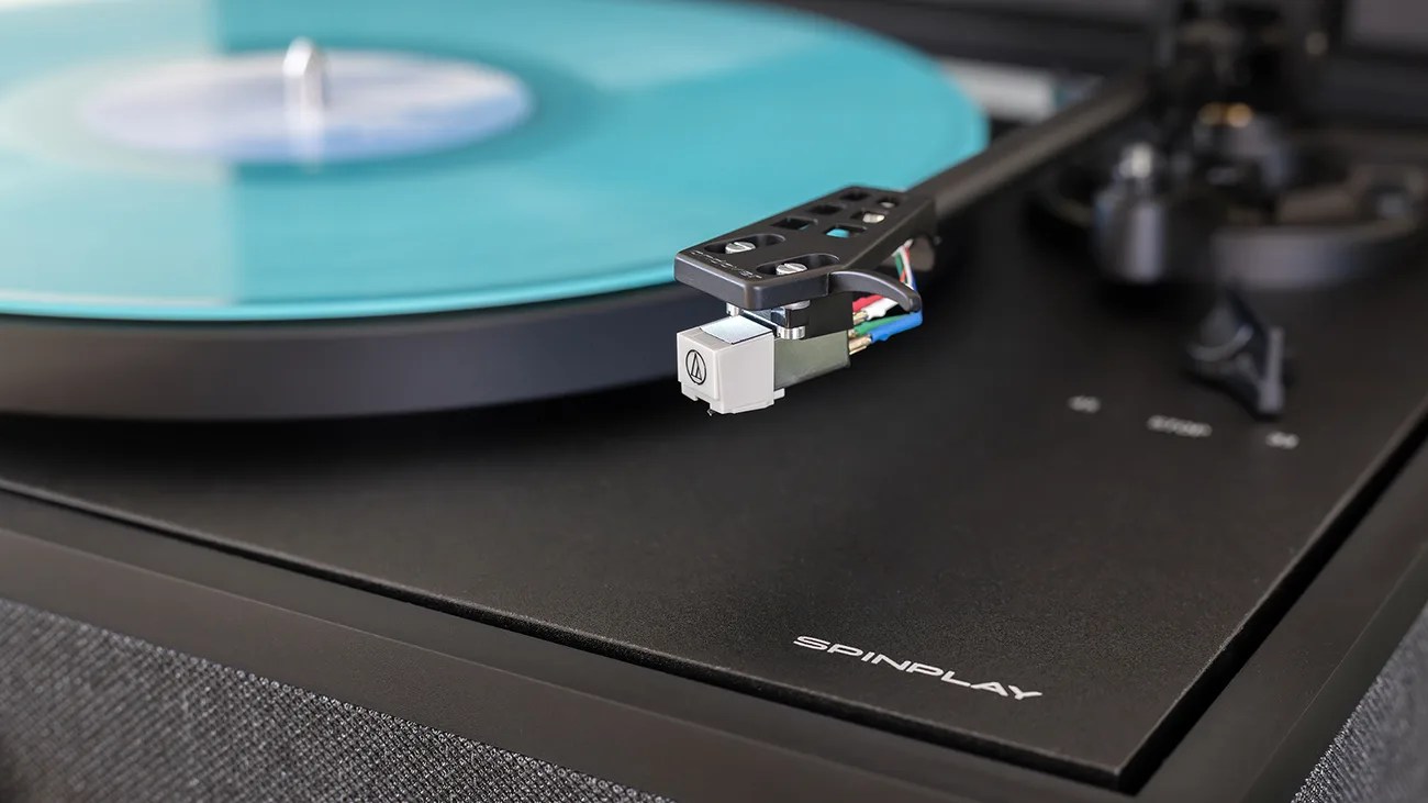 Close-up of a black SpinPlay turntable with a turquoise vinyl record and Audio-Technica cartridge on the tonearm.