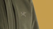 Olive green fleece jacket with a white embroidered skeletal bird logo on the chest.