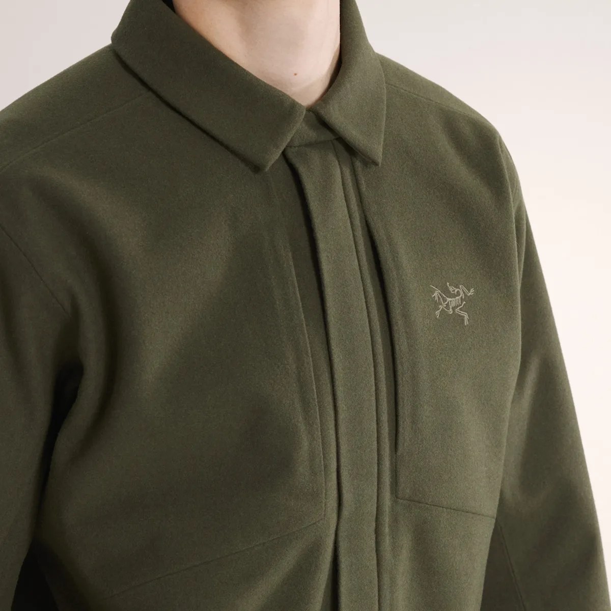 Olive green jacket with a hidden front zipper and embroidered logo on the chest.