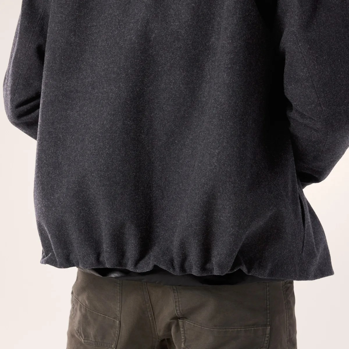 Back view of a person wearing a dark gray wool jacket with elastic hem and olive green pants.
