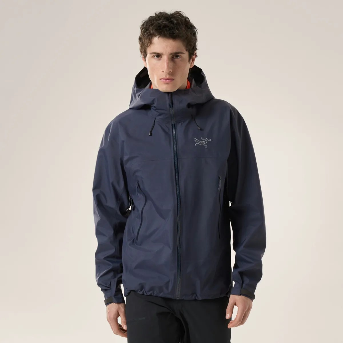 Navy blue hooded waterproof jacket with front zipper and logo on chest worn by a person.
