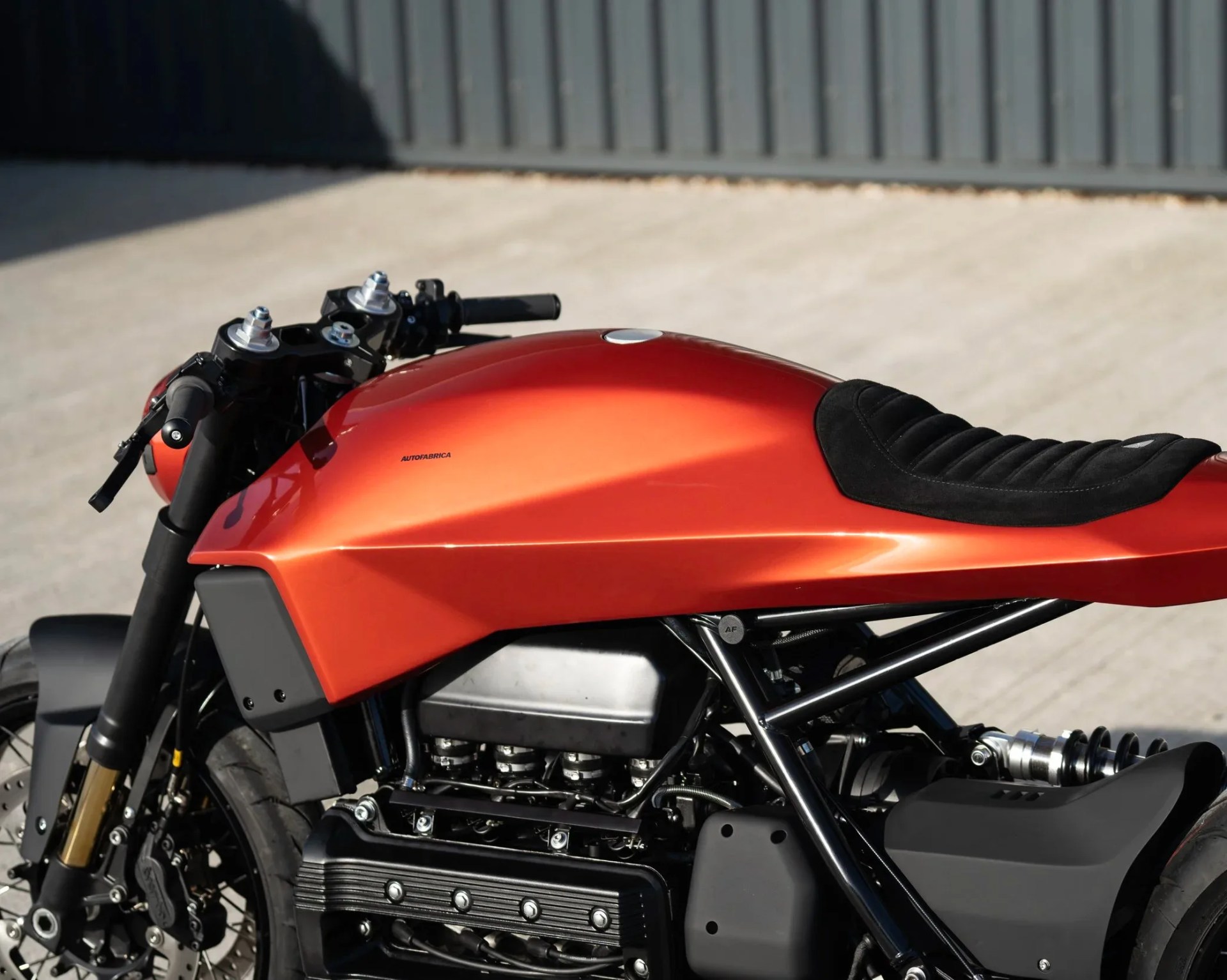 Orange motorcycle fuel tank with black suede seat and visible engine components.