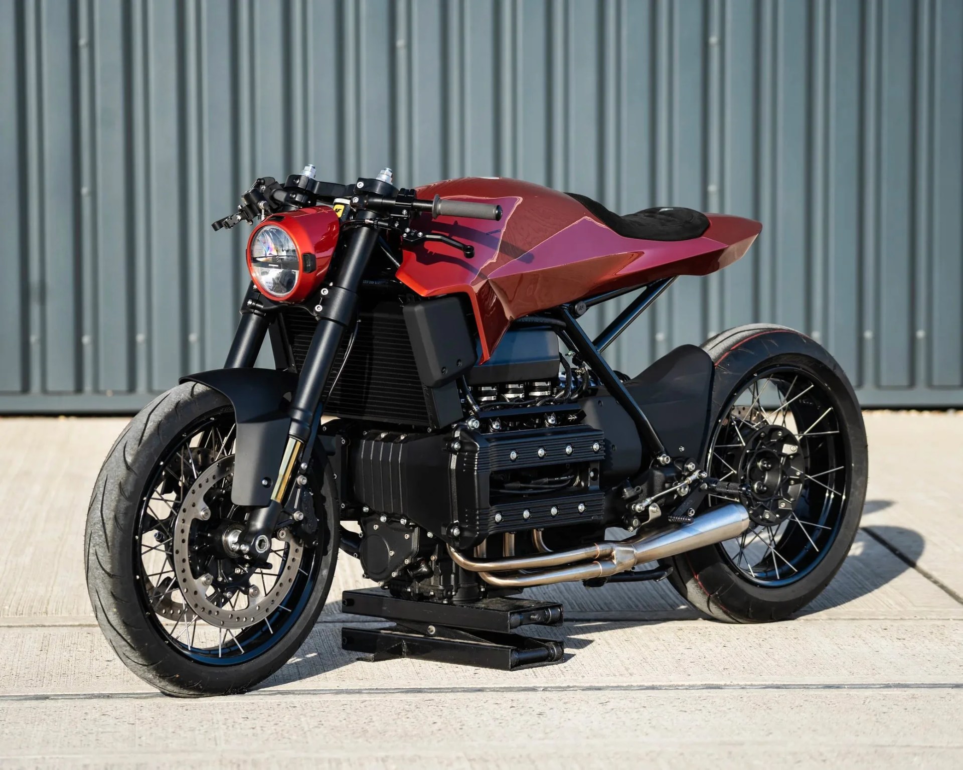 Custom cafe racer motorcycle with a red angular fuel tank, black frame, and exposed engine on a concrete surface.