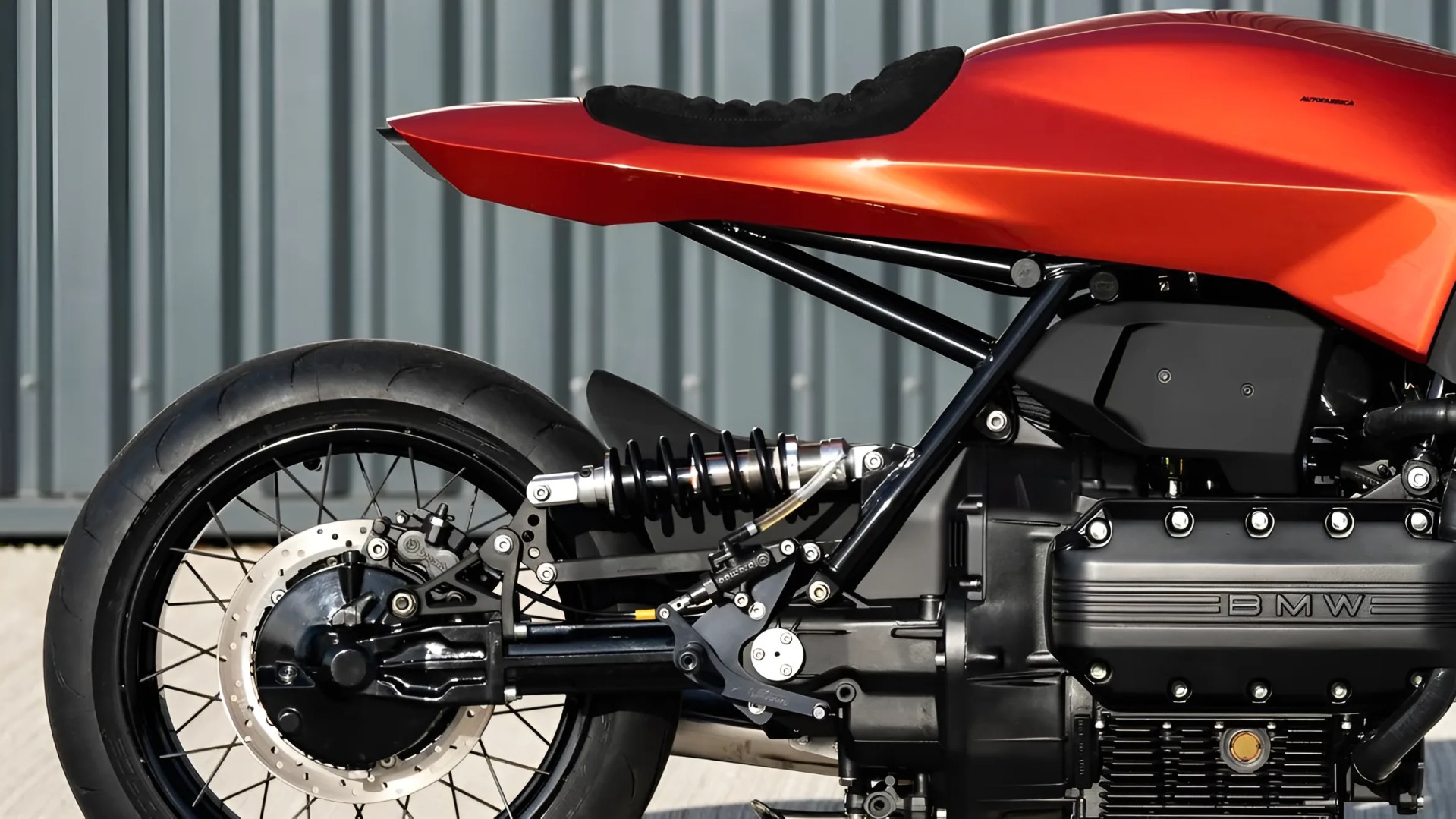Close-up of the rear section of a black and orange BMW motorcycle showing the rear wheel, suspension, and part of the engine.