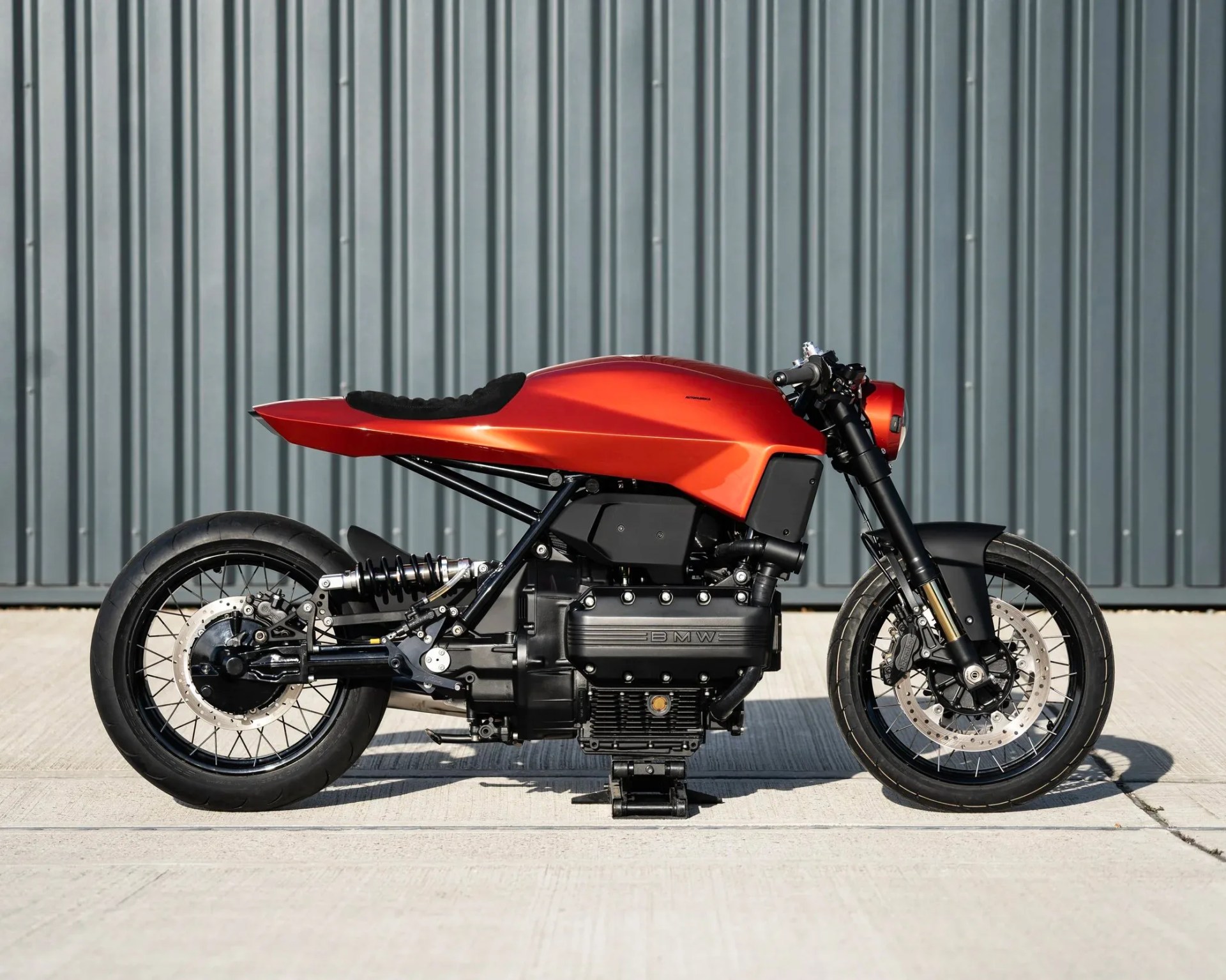 Custom cafe racer motorcycle with a matte orange fuel tank and black frame parked on concrete.