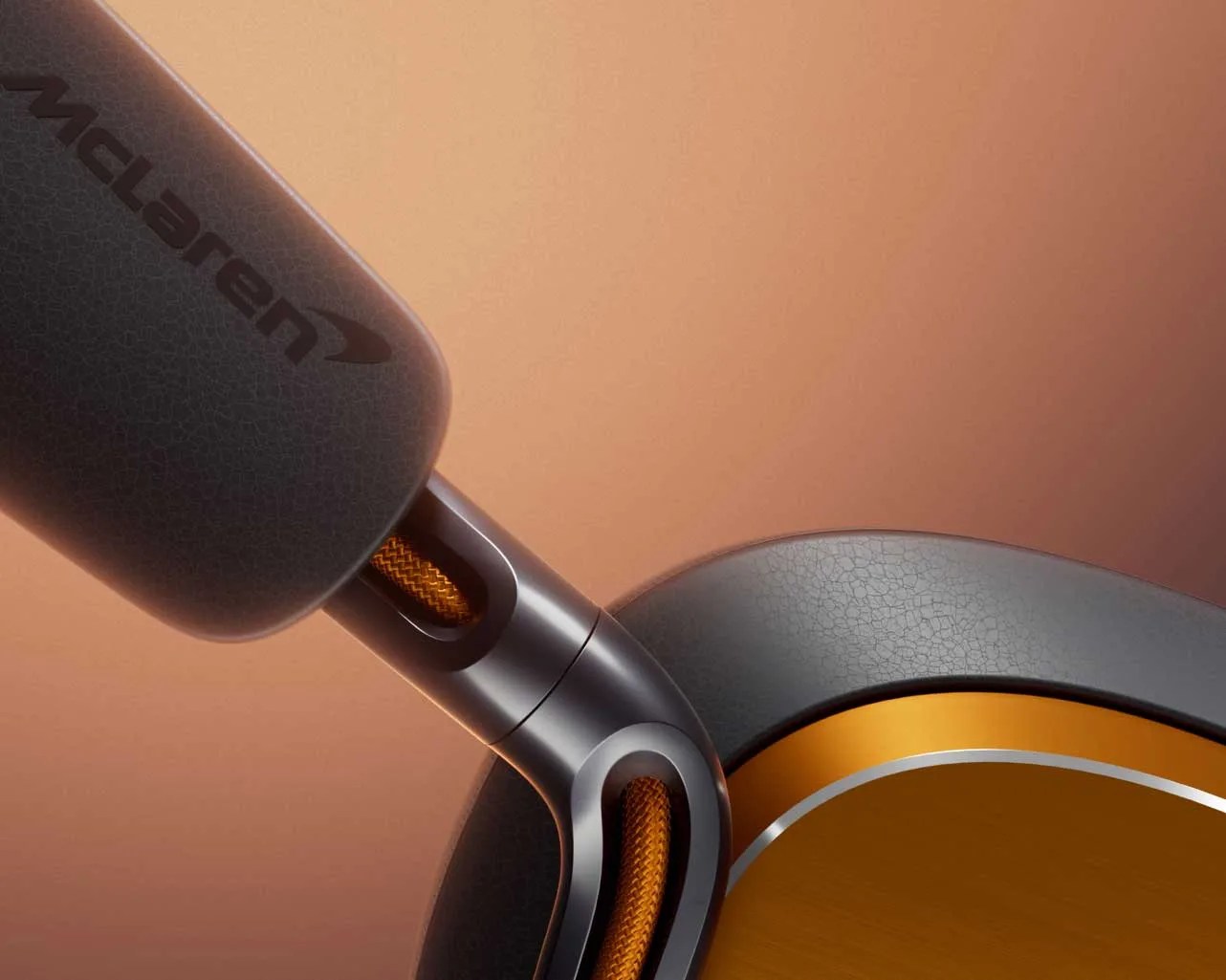Close-up of a McLaren-branded headphone arm with black and orange braided cable and metallic orange ear cup.