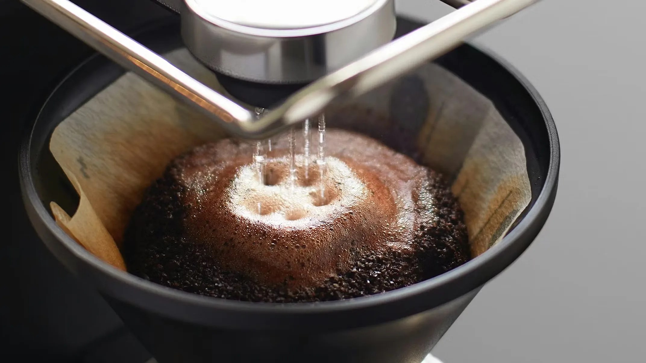 Close-up of water dripping from a coffee maker onto wet coffee grounds in a paper filter inside a black coffee dripper.