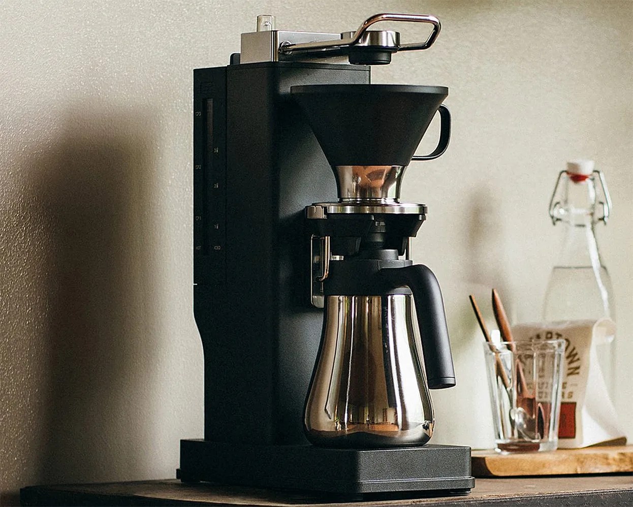 Black and stainless steel drip coffee maker with a glass carafe on a wooden countertop.