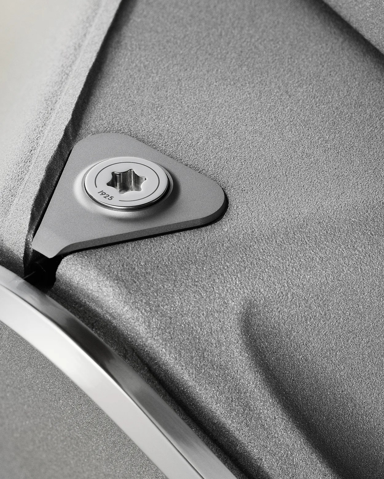 Close-up of a textured gray metal surface with a triangular metal plate and a star-shaped screw marked "1925.