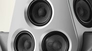 Close-up of a silver speaker panel with four black speaker cones surrounded by concentric silver rings.