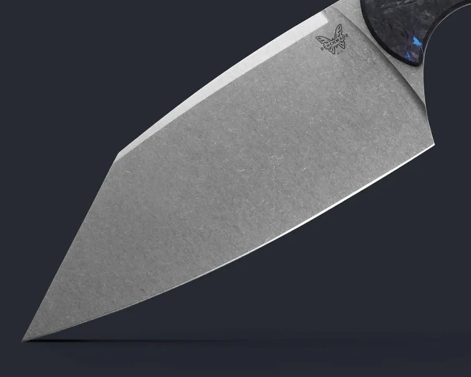 Close-up of a gray knife blade with a butterfly logo near the handle on a dark background.