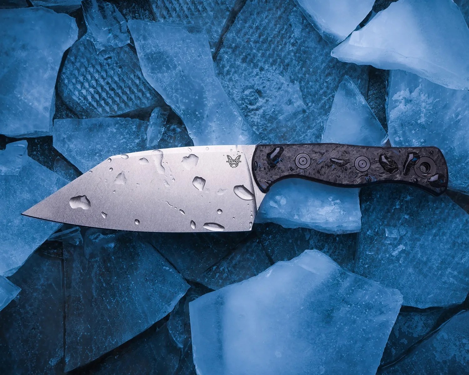 Knife with a broad silver blade and dark textured handle resting on cracked blue ice.