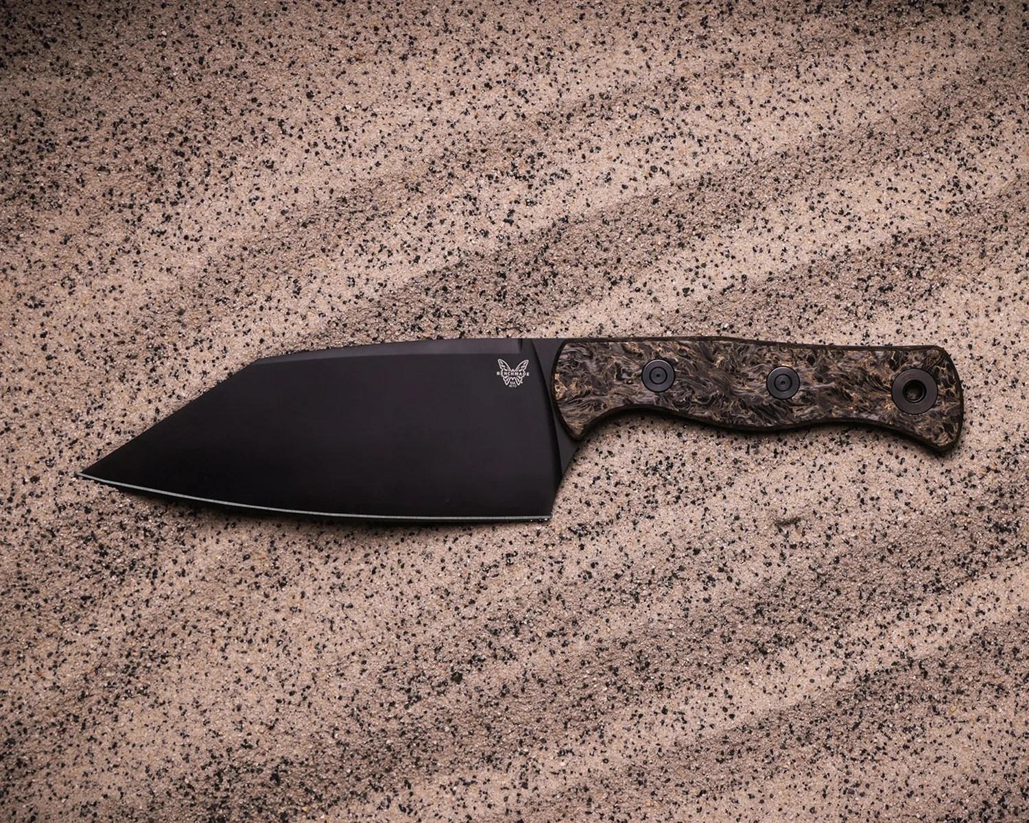 Black fixed-blade knife with a textured brown handle on a speckled surface.