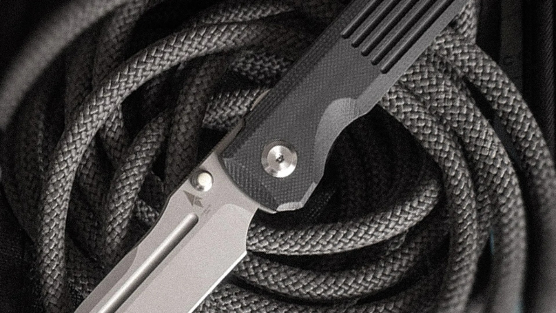 Close-up of a folding knife with a textured black handle resting on coiled black rope.