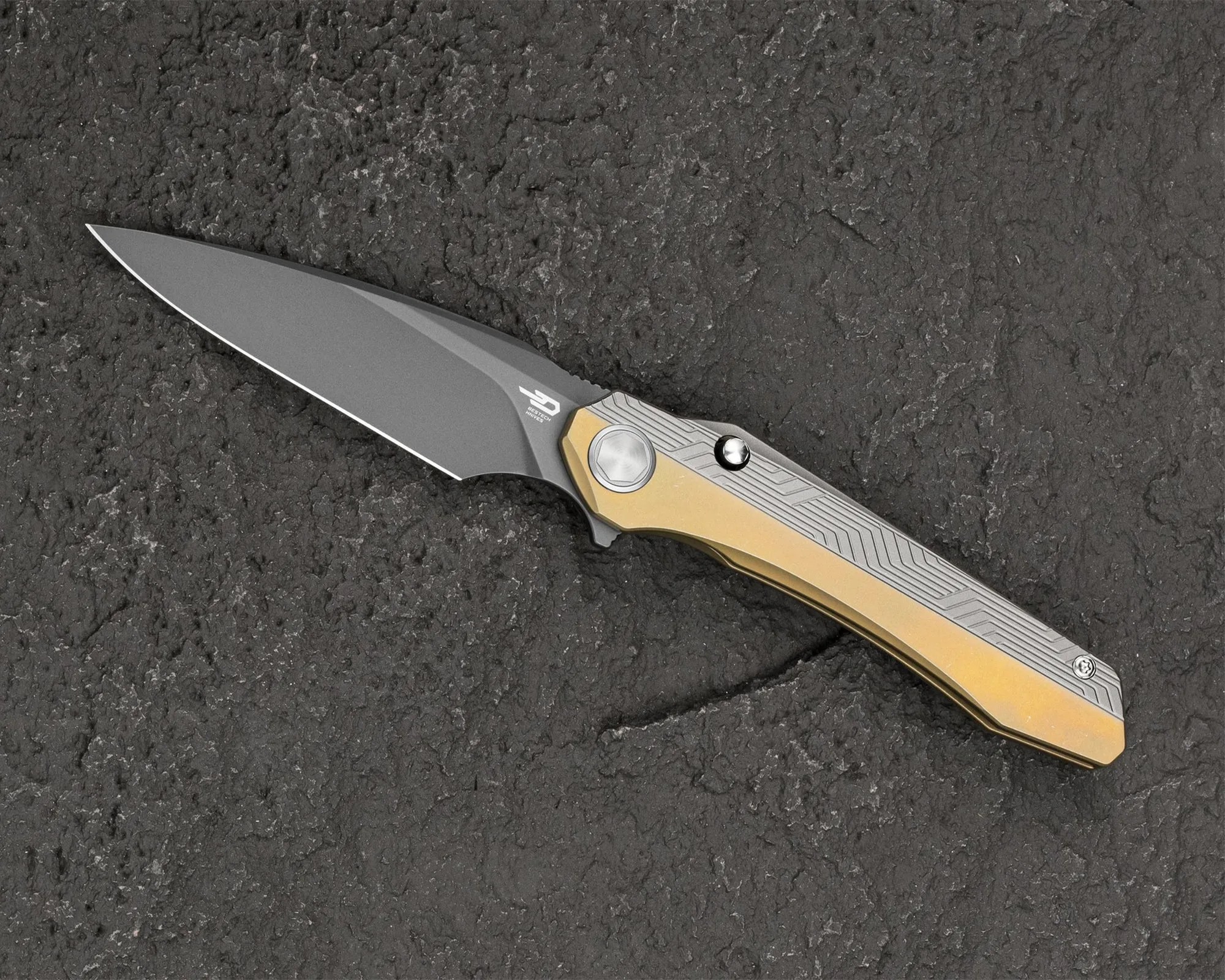 Folding knife with a gray blade and a gold and silver patterned handle on a textured dark surface.