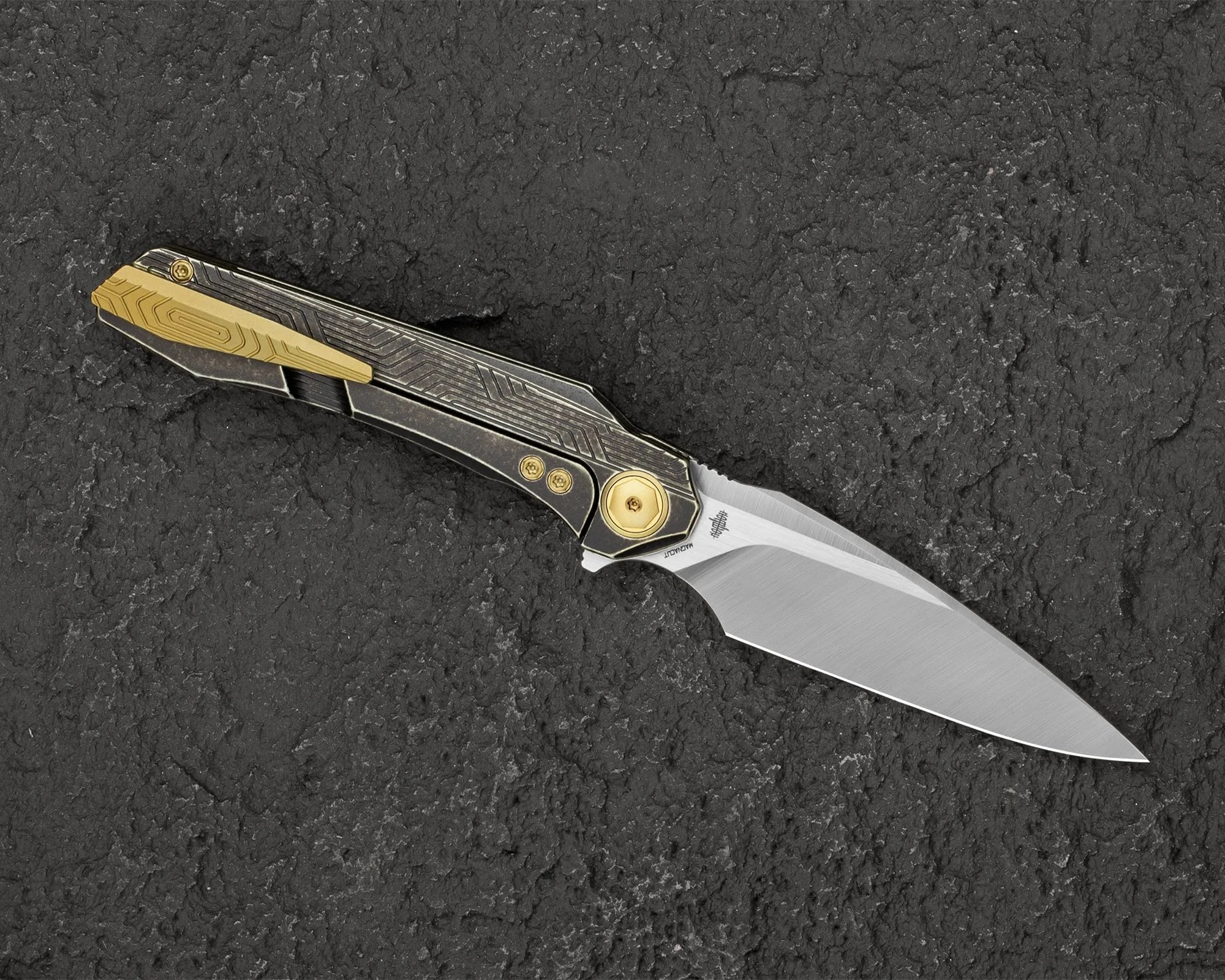 Folding knife with a silver blade and black handle featuring gold accents on a textured dark surface.