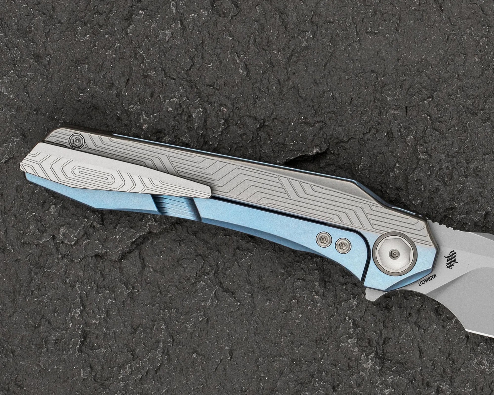 Blue and silver folding knife handle with geometric line patterns on a textured dark surface.
