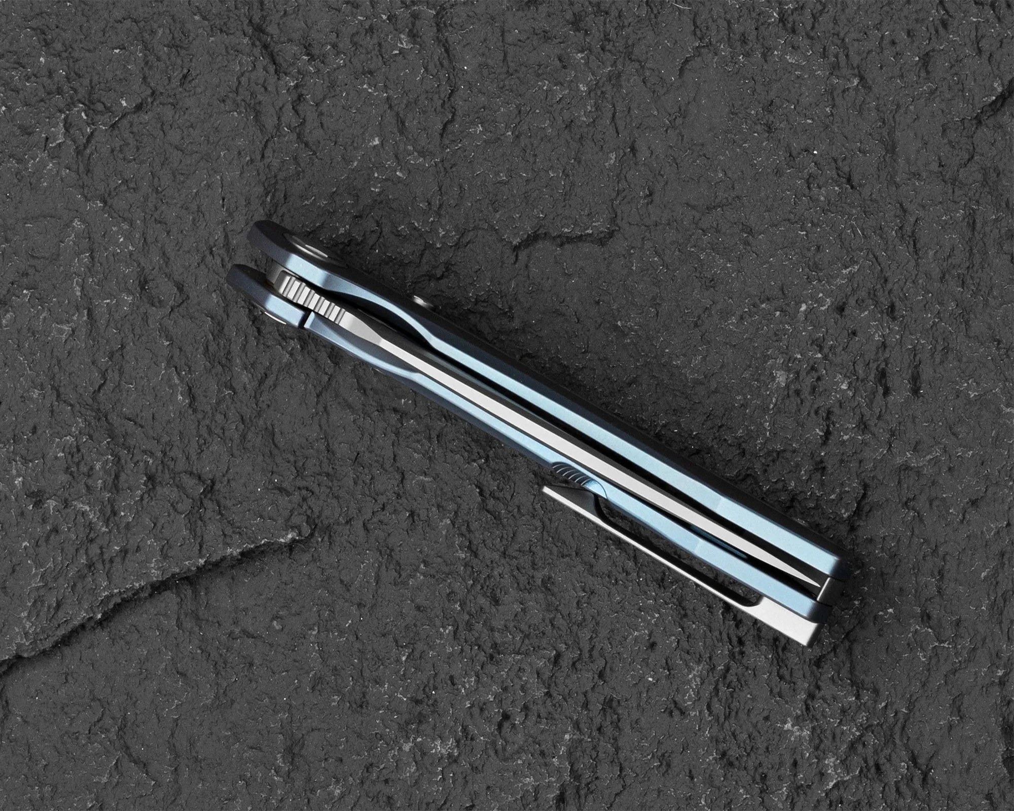 Closed blue folding knife with a metal clip on a textured dark surface.