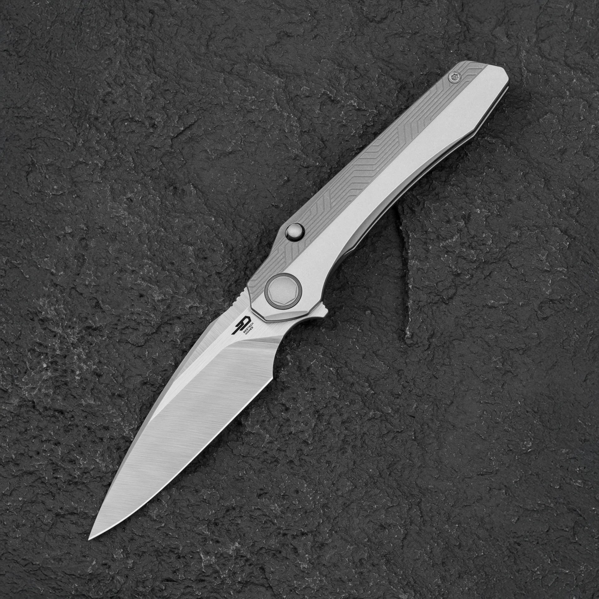 Silver folding knife with a textured handle and a sharp, pointed blade on a black textured surface.