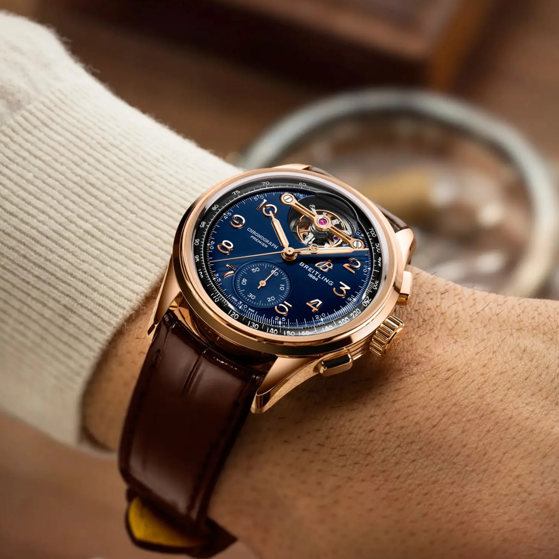 Rose gold Breitling chronograph watch with blue dial and brown leather strap worn on a wrist.